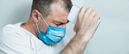 man with mask holding a phone up to his forehead